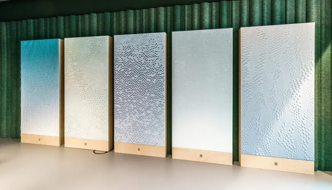 Five vertical light panels with varying shades and patterns of blue and white, mounted on a wooden base, displayed against a dark green curtain backdrop. Each panel illuminates unique textured effects, ideal for enhancing the An image from EDGE Workspaces.