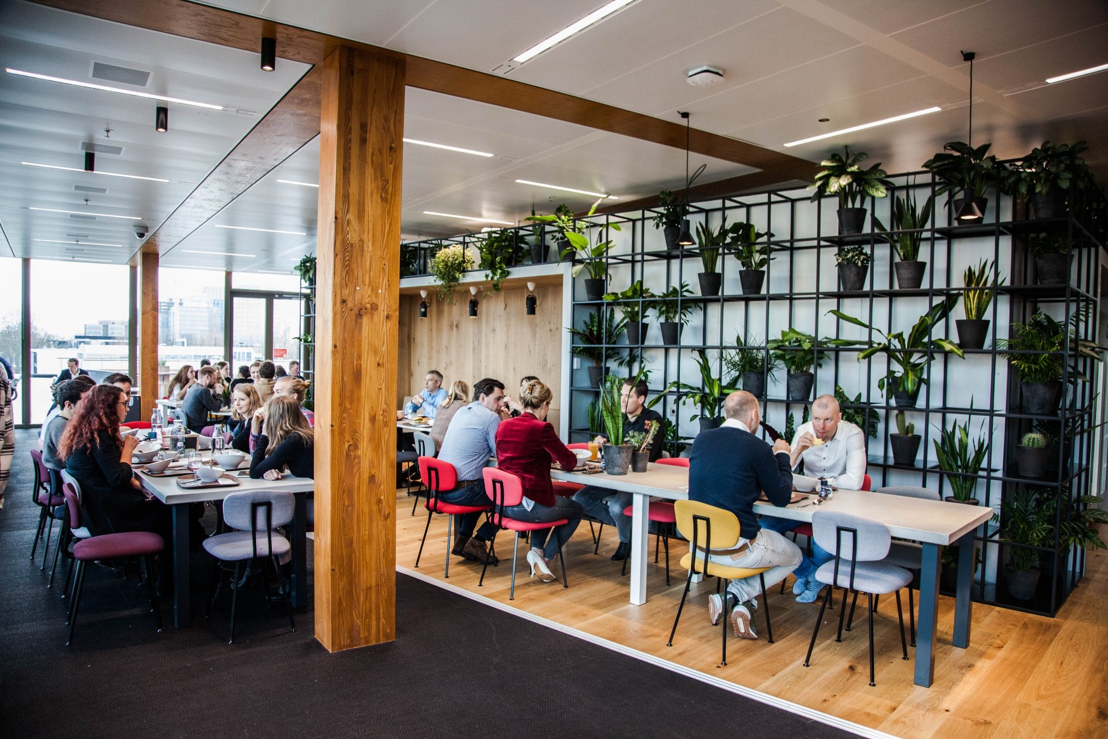 A modern coworking space with walls adorned by vertical gardens. People, dressed in casual and business attire, are engaged in discussions while sitting at various tables. The room features large windows and sleek, contemporary An image from EDGE Workspaces.