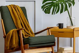 A cozy nook in an innovative coworking environment, featuring a modern wooden armchair with a green cushion and a yellow throw blanket, beside a small wooden table with a black mug and a clear vase An image from EDGE Workspaces.